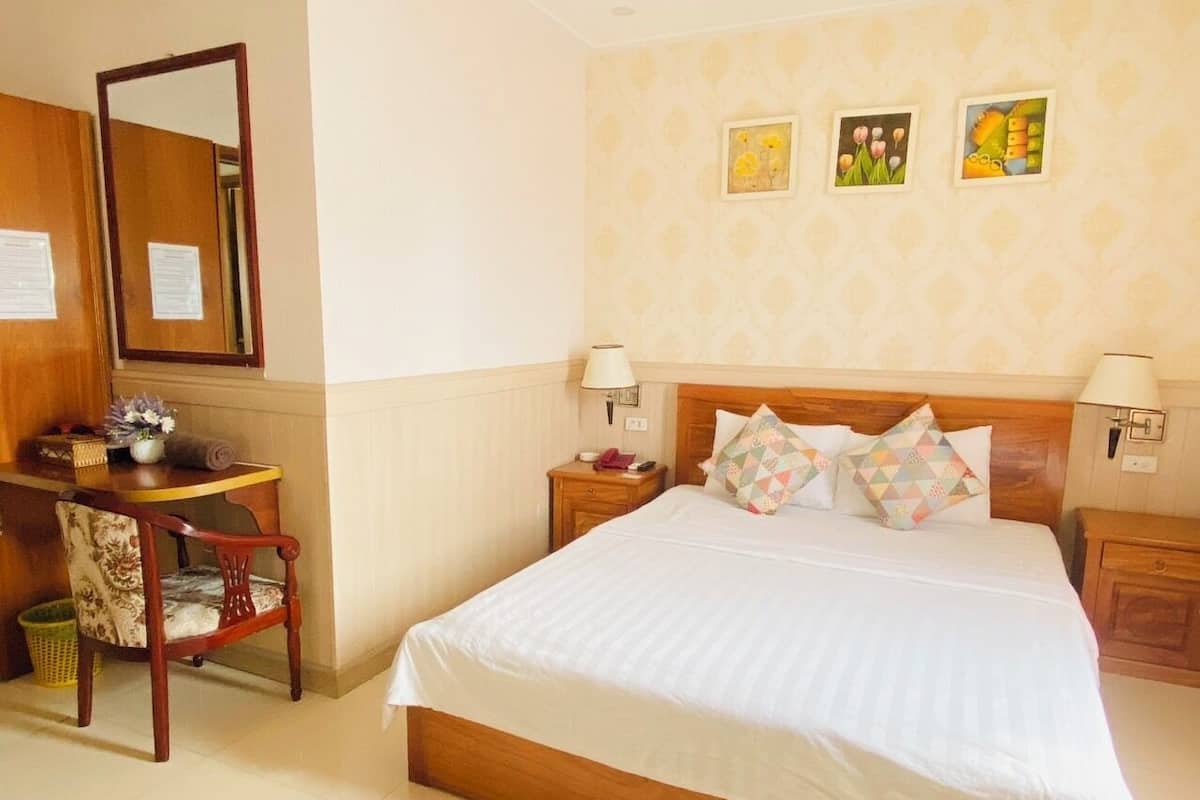 Ein Hotelzimmer mit einem großen Bett, zwei Nachttischen, einem hölzernen Beistelltisch, einem Sessel, einem kleinen Tisch mit Lampe und einem Spiegel.