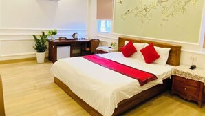 A hotel room with a large bed, a desk, a chair, a small table, and a potted plant. - Nhu Y Hotel (Ho Chi Minh City)