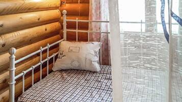 A wooden cabin room with a metal bed frame, a checkered bedspread, and a single pillow.