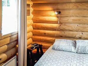 L’intérieur d’une cabane en bois, avec un lit, une petite table et une fenêtre.