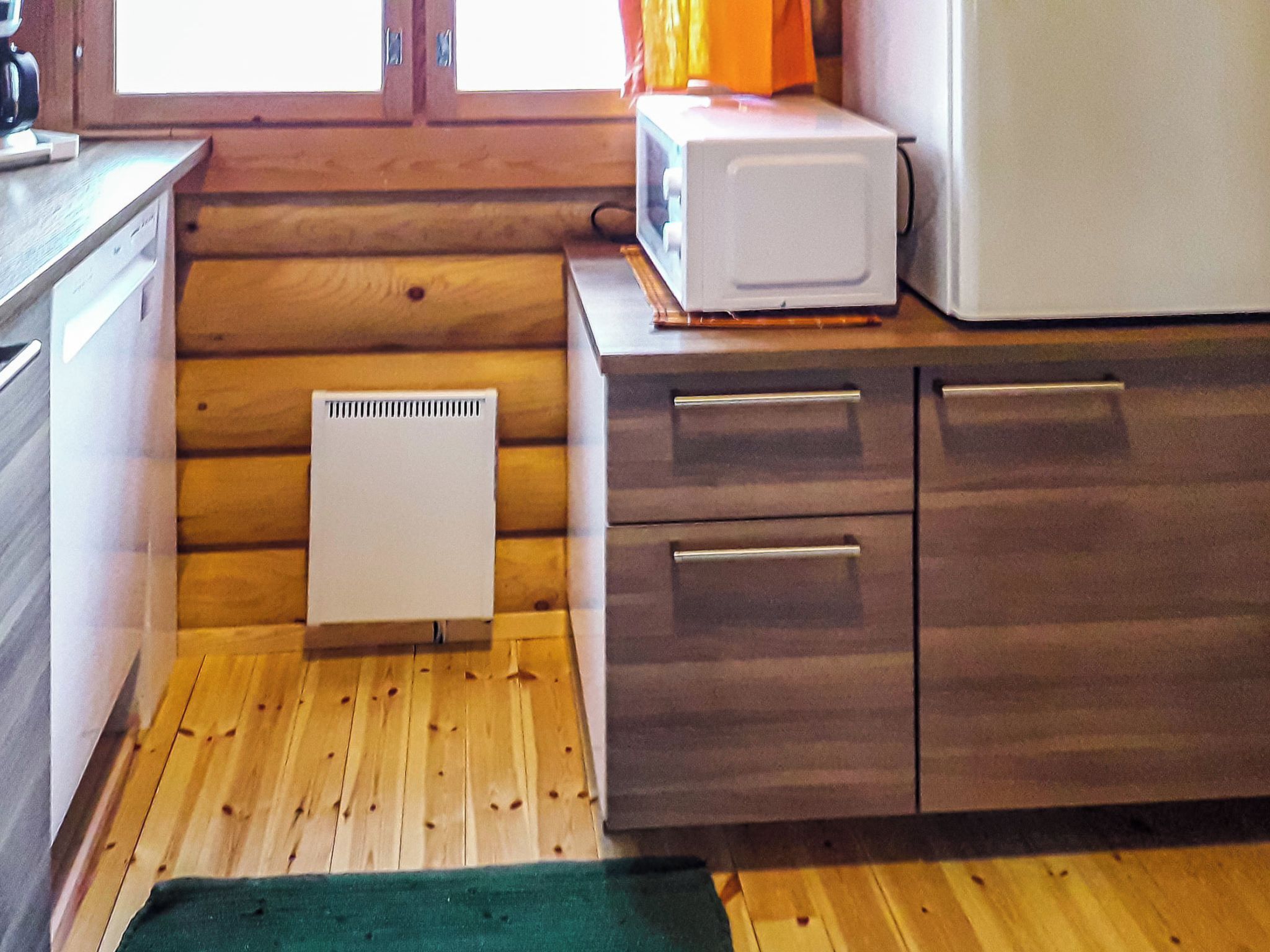 A compact kitchen with wooden walls, a white radiator, and a microwave on the countertop.