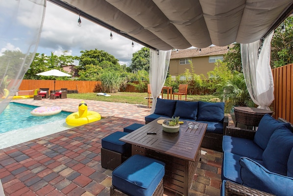 An outdoor patio with a pool, seating area, and a covered section.
