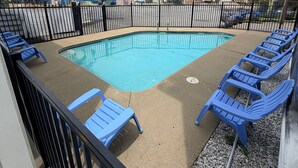 Una piscina con sillas azules a su alrededor, rodeada por una valla negra.
