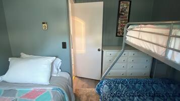 A bedroom with two beds, a dresser, and a door leading to another room.