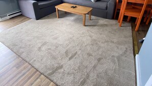Una sala de estar con un sofá modular, una mesa de centro, un ventilador de techo y un comedor con sillas.