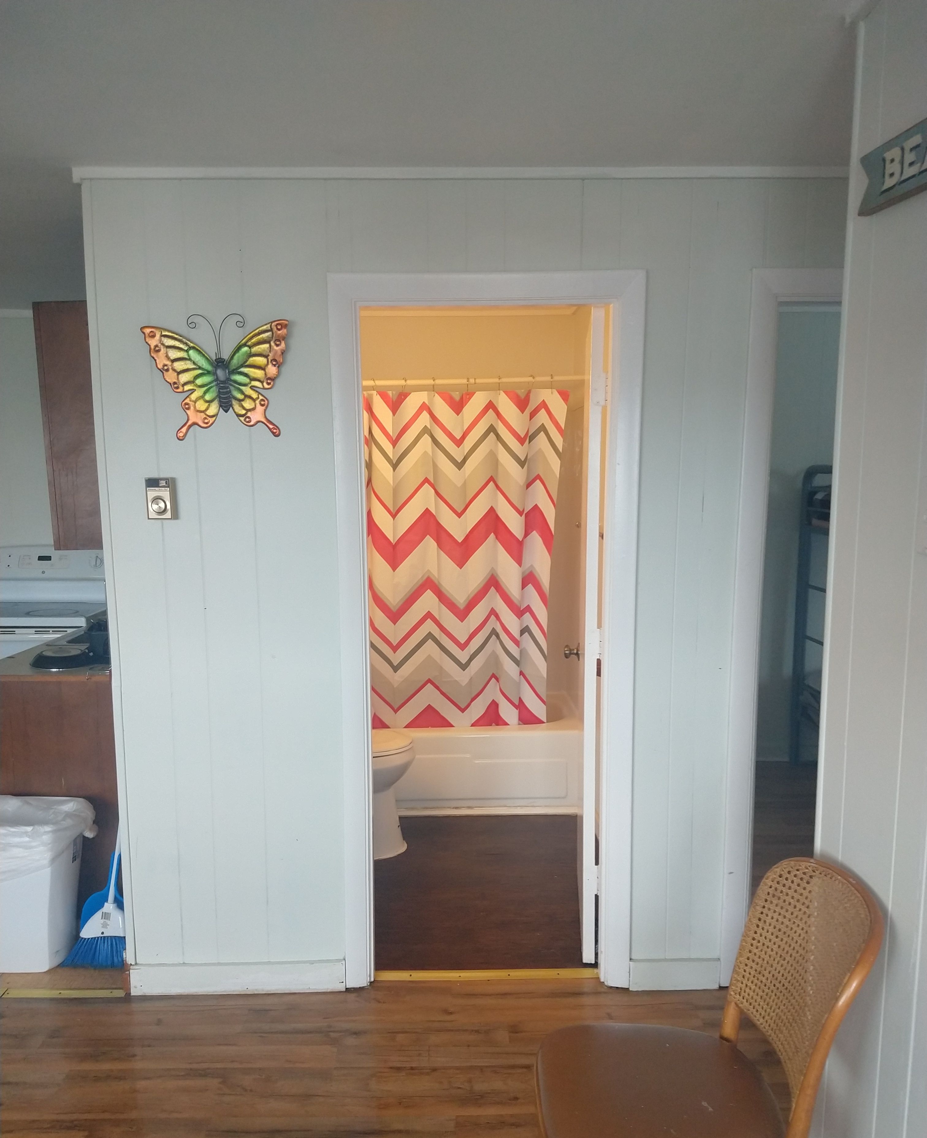 Un baño con cortina de ducha estampada en patrón geométrico de chevron, un inodoro y piso de madera.