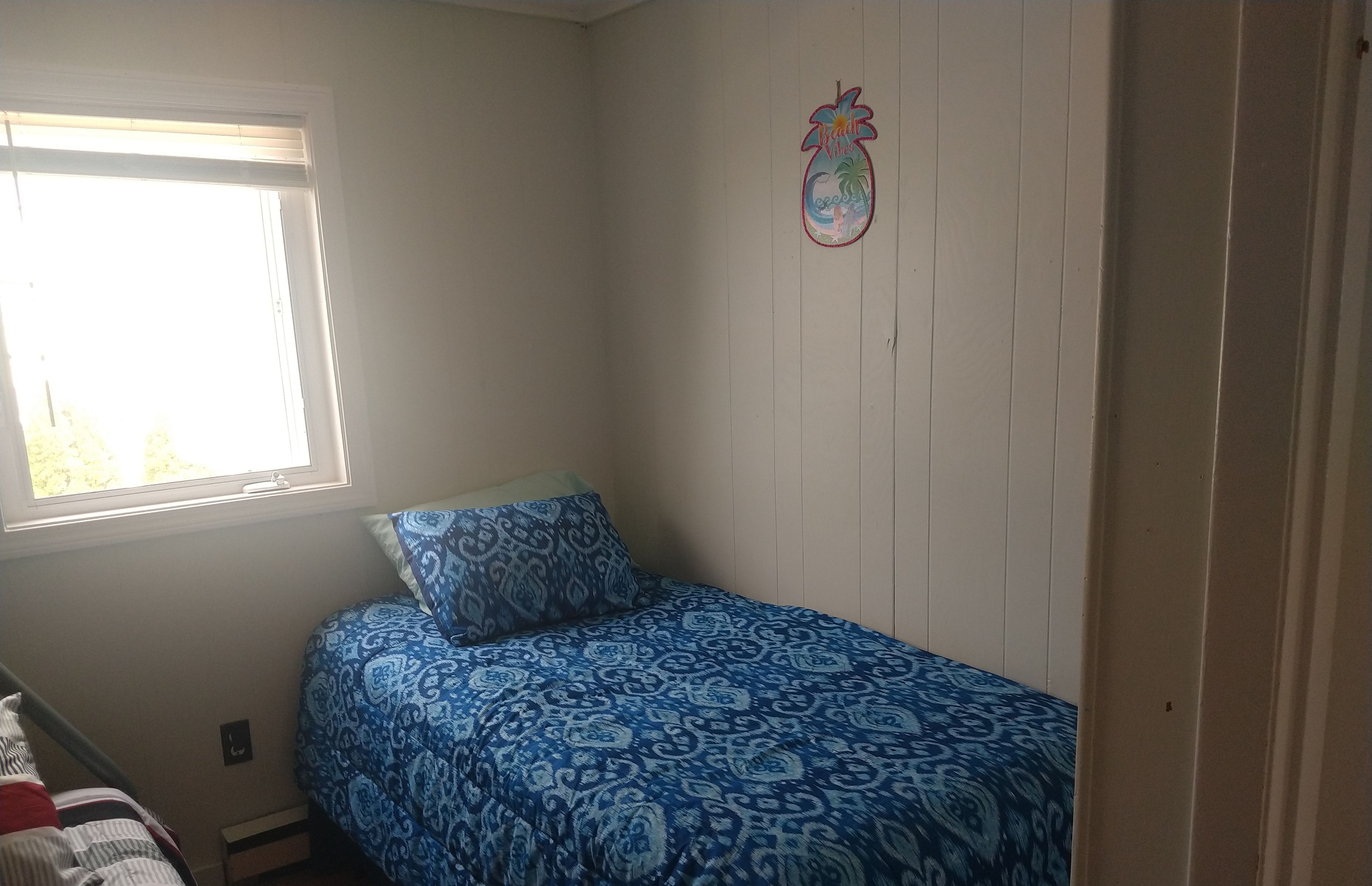 A small, sparsely furnished room with a single bed, a window, and a wall decoration.