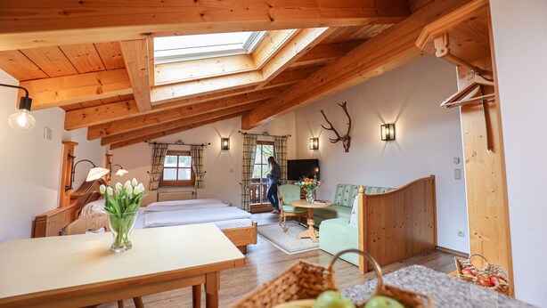 Une pièce chaleureuse avec un plafond en bois, un lit, une table ornée d’un vase de fleurs et un téléviseur.