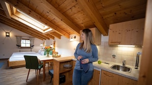 Ein gemütliches Zimmer mit einem Bett, einem Esstisch mit Stühlen, einer Küchenzeile mit Holdekor und einem Spülbecken sowie einem Oberlicht.