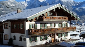 Ein traditionelles Chalet mit Balkon, vor einer Kulisse schneebedeckter Berge.