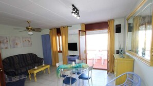 A living room with a sofa, a dining table with chairs, a ceiling fan, and a large mirror. - AP FLAMENC, Ideal house for your holidays near the sea, free wifi, air conditioning optional, pets allowed, dog’s beach (Delta de l'Ebre)