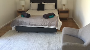 A neatly arranged bedroom with a bed, bedside tables, a chair, and a rug. - Swansea Lakeside Retreat is a large property on the shores of Lake Macquarie (Swansea)