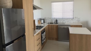 A modern kitchen with stainless steel appliances, wooden cabinets, and a window with blinds. - Swansea Lakeside Retreat is a large property on the shores of Lake Macquarie (Swansea)