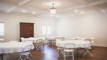 A conference room with multiple tables and chairs, wooden flooring, and a chandelier.