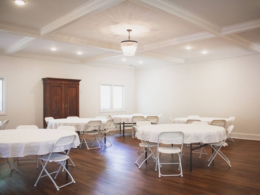 A conference room with multiple tables and chairs, wooden flooring, and a chandelier.