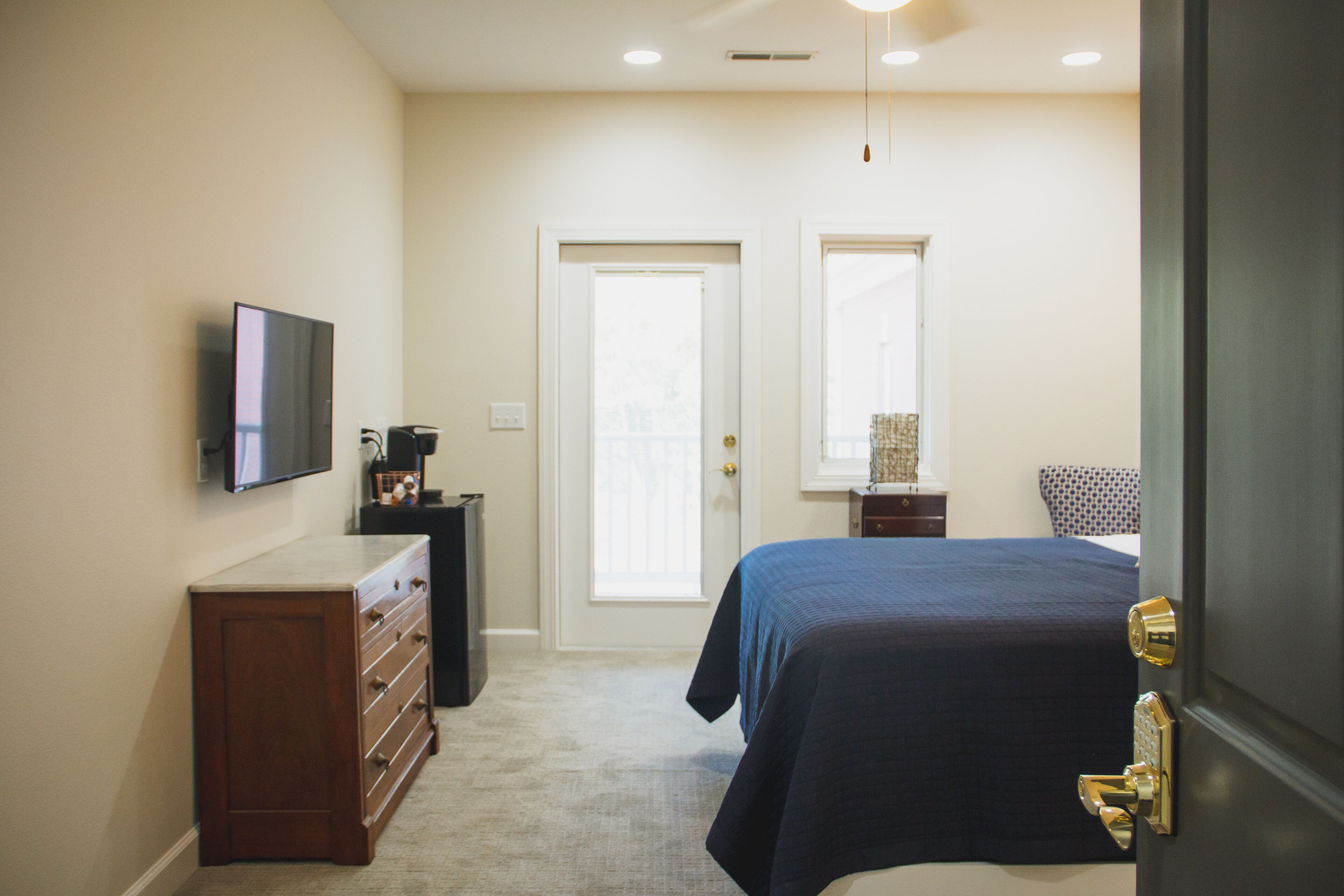 A bedroom with a bed, a dresser, a television, and a door leading to another room.