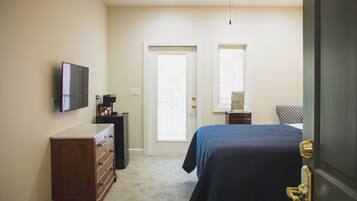 A bedroom with a bed, a dresser, a television, and a door leading to another room.