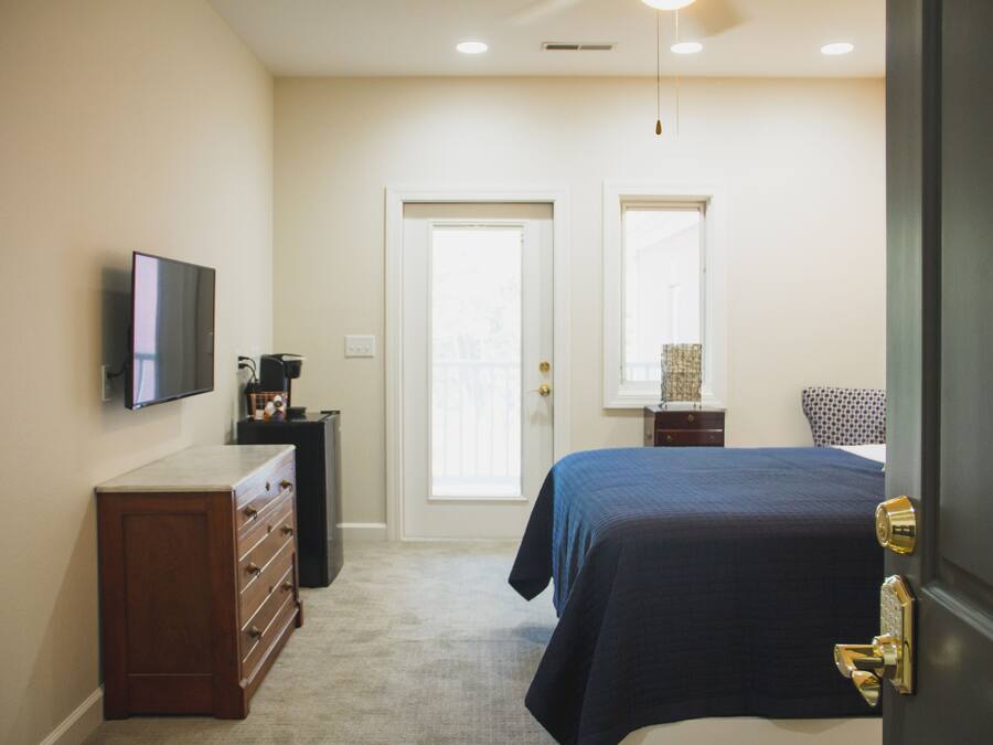 A bedroom with a bed, a dresser, a television, and a door leading to another room.