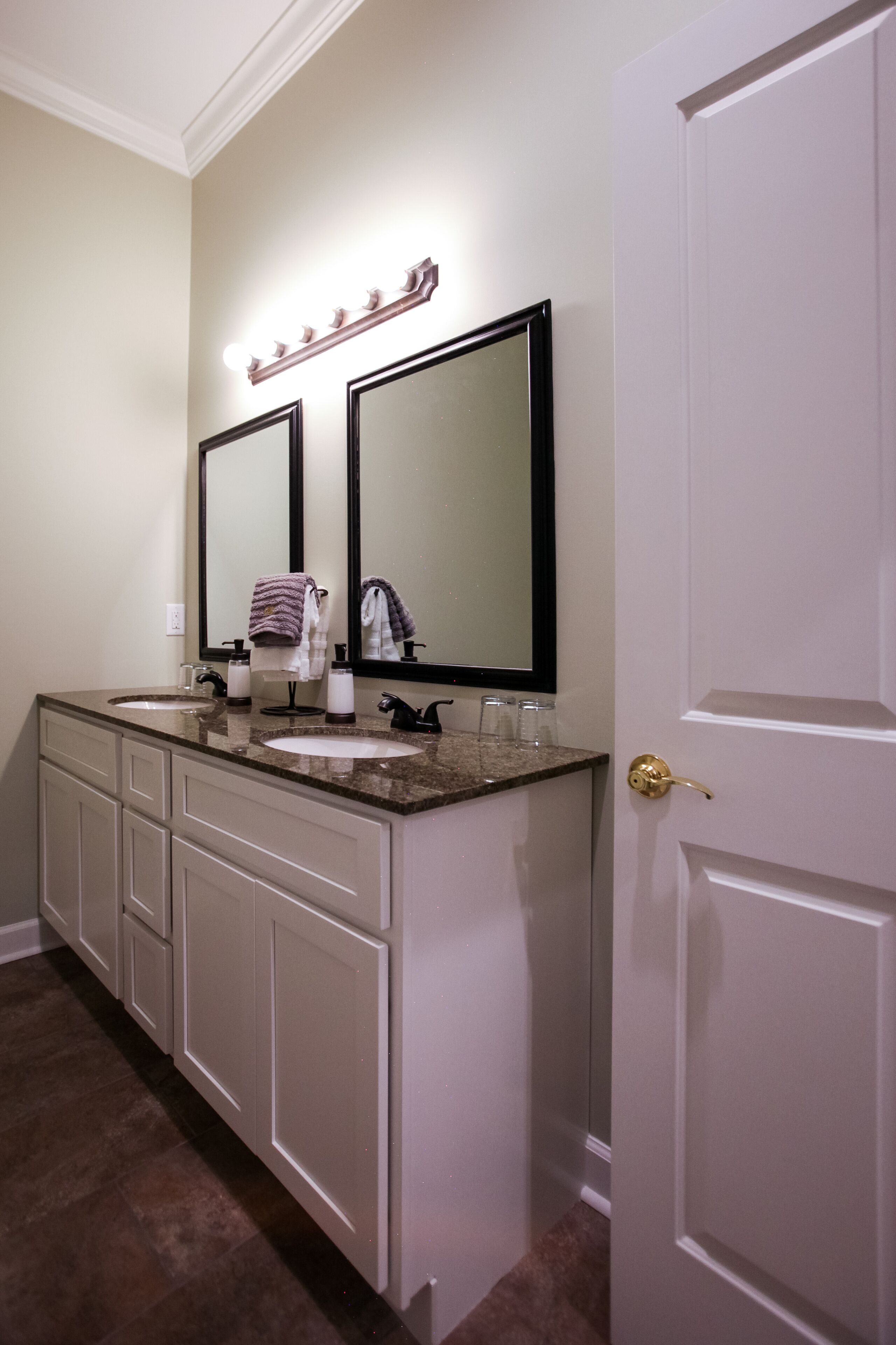 A bathroom with two sinks, a vanity with drawers, a large mirror, and a door with a golden handle.