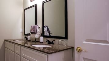 A bathroom with two sinks, a vanity with drawers, a large mirror, and a door with a golden handle.