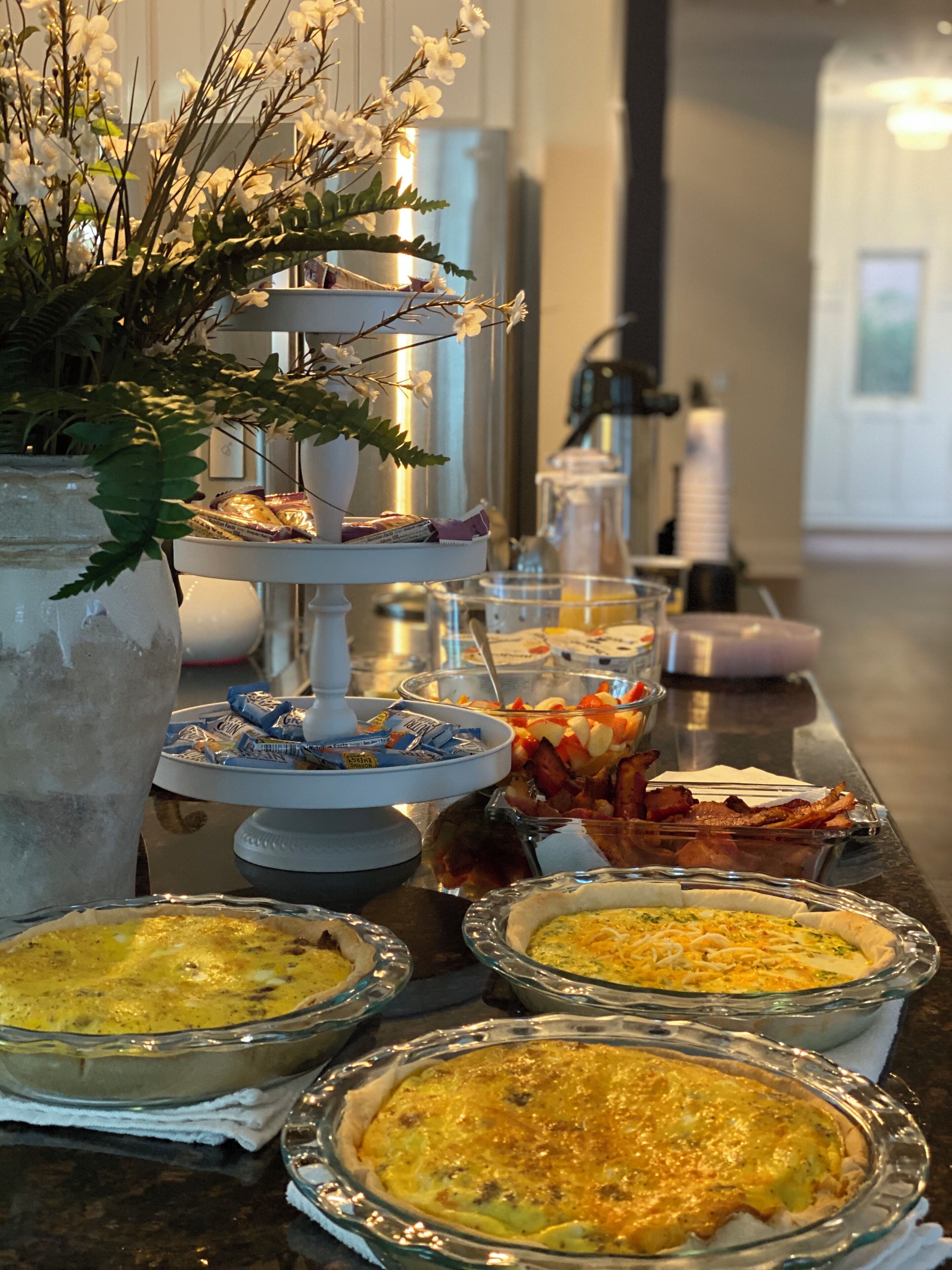 A buffet table with various dishes, including quiches and bacon, and a decorative plant in the foreground.