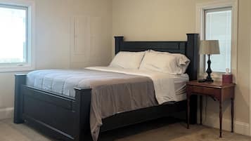 Un dormitorio con una cama, una mesita de noche, una lámpara y una ventana.