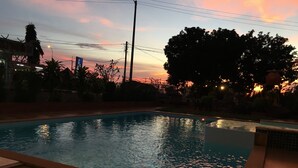 Piscina com deck ladrilhado, cercada por árvores e uma cerca.