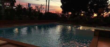 A swimming pool with a tiled deck, surrounded by trees and a fence.