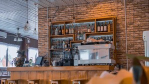 Uma área de bar com banquetas de madeira, uma máquina de café e prateleiras cheias de garrafas.
