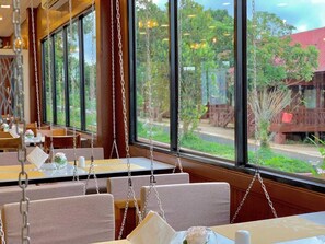 En restaurang med en inredning som inkluderar hängande sittplatser och stora fönster som ger utsikt över omgivningen.
