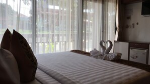 Quarto de hotel com cama, almofadas, escrivaninha, frigorífico e cortinas translúcidas.