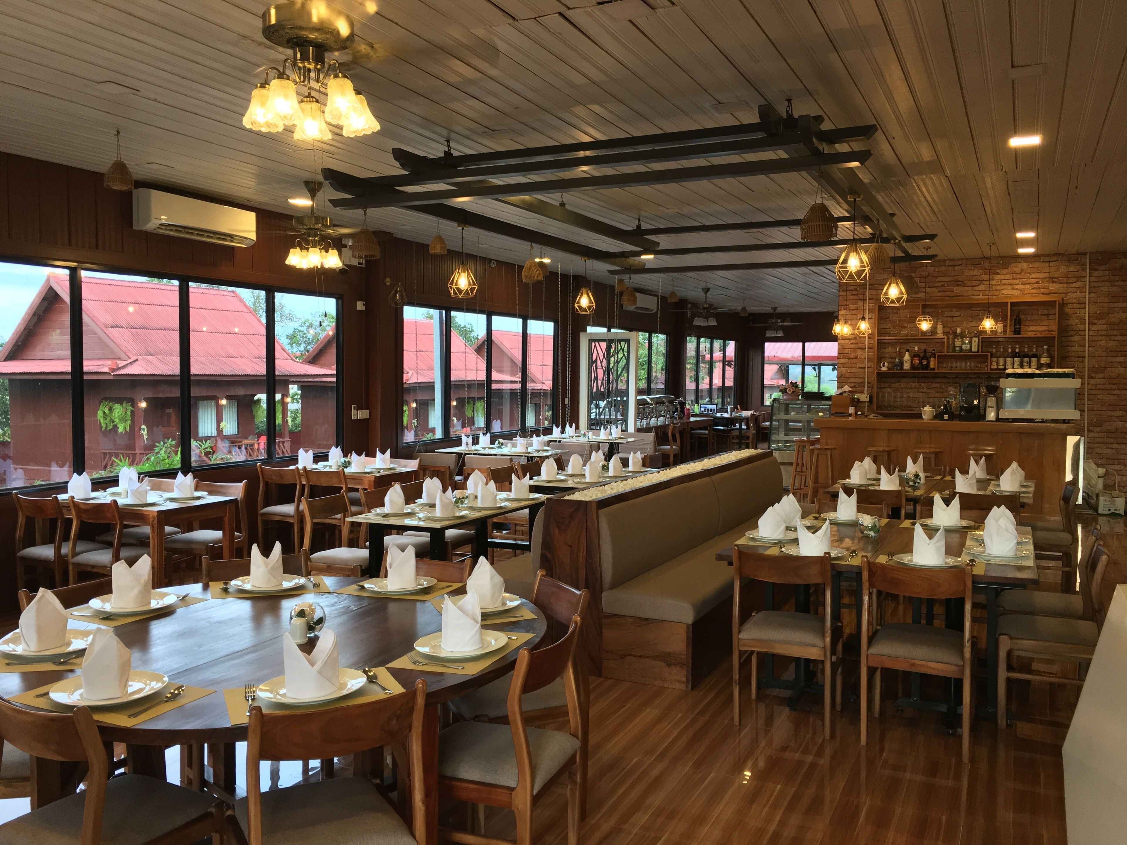 Un ristorante con tavoli e sedie in legno, un'area bar e ampie finestre che offrono vista sugli edifici esterni.