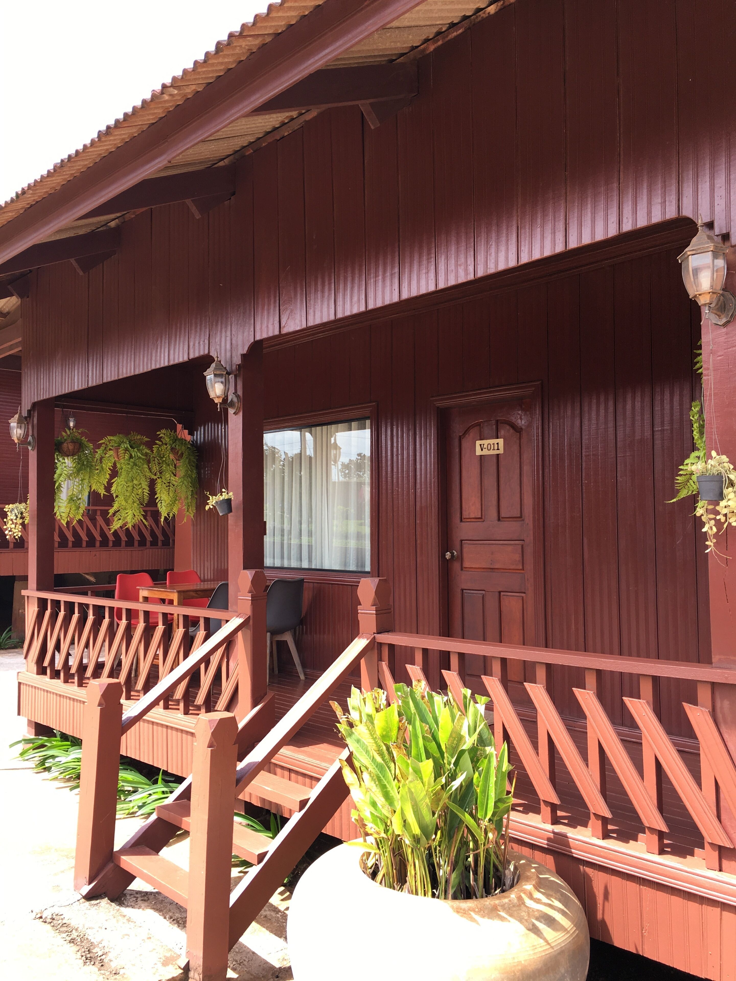A wooden building with a porch, a door labeled "V-011", and a potted plant in the foreground.