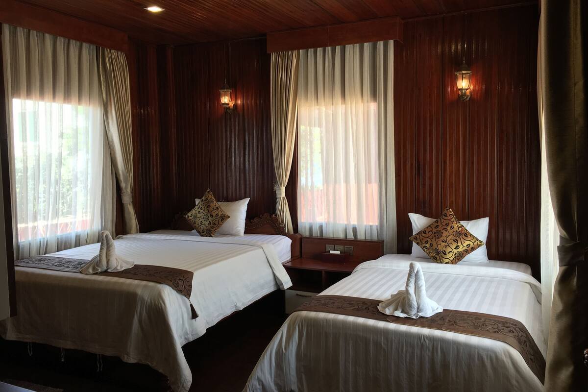 A hotel room with two beds, wooden paneling, and two wall-mounted lamps.