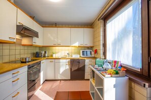 A kitchen with white cabinets, a stove, an oven, a microwave, and a window with curtains. - Chiara's Home, Pregassona (Lugano), Switzerland (Pregassona (Lugano))