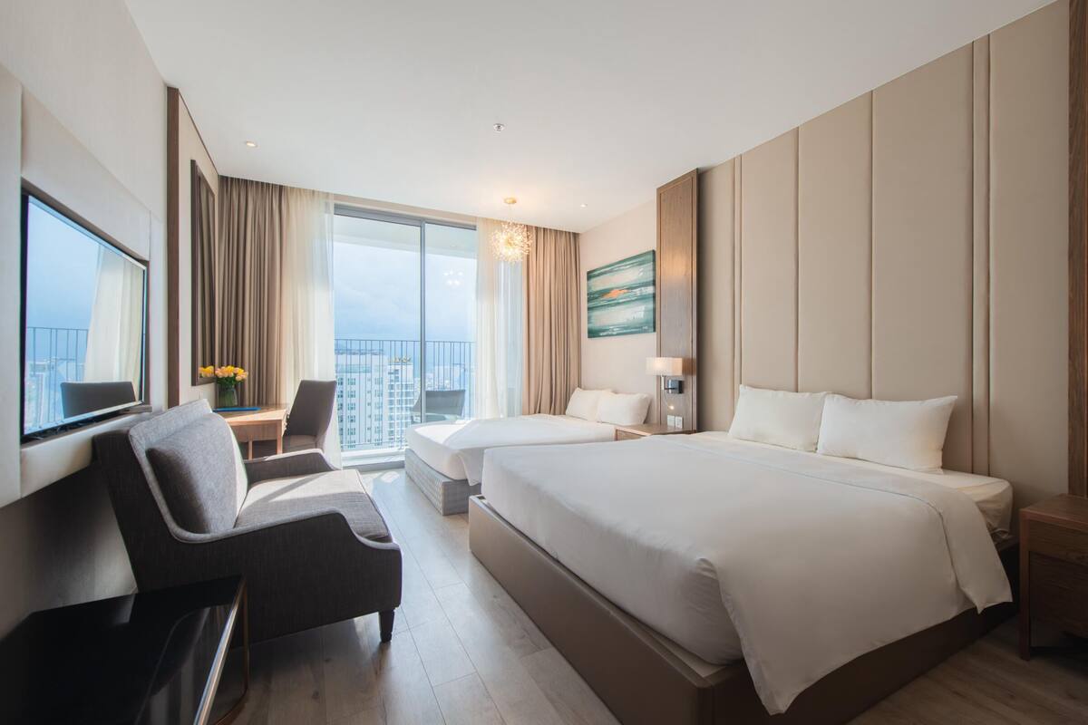 Een moderne hotelkamer met twee bedden, een bureau, een stoel en een groot raam met uitzicht op de stad.