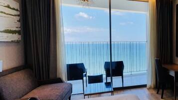 Quarto de hotel com uma cama grande, uma mesa de trabalho e vista para o mar através de uma porta deslizante.