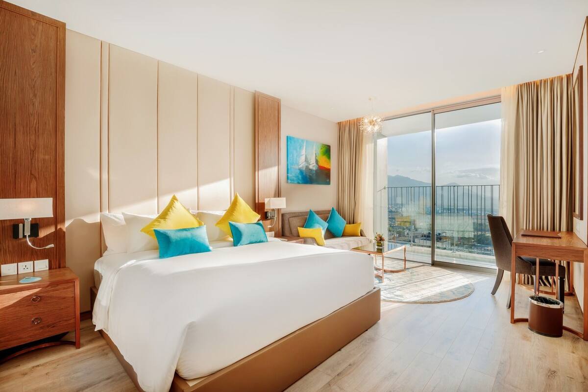 Een moderne hotelkamer met een groot bed, een bureau en een balkon met uitzicht over de stad.