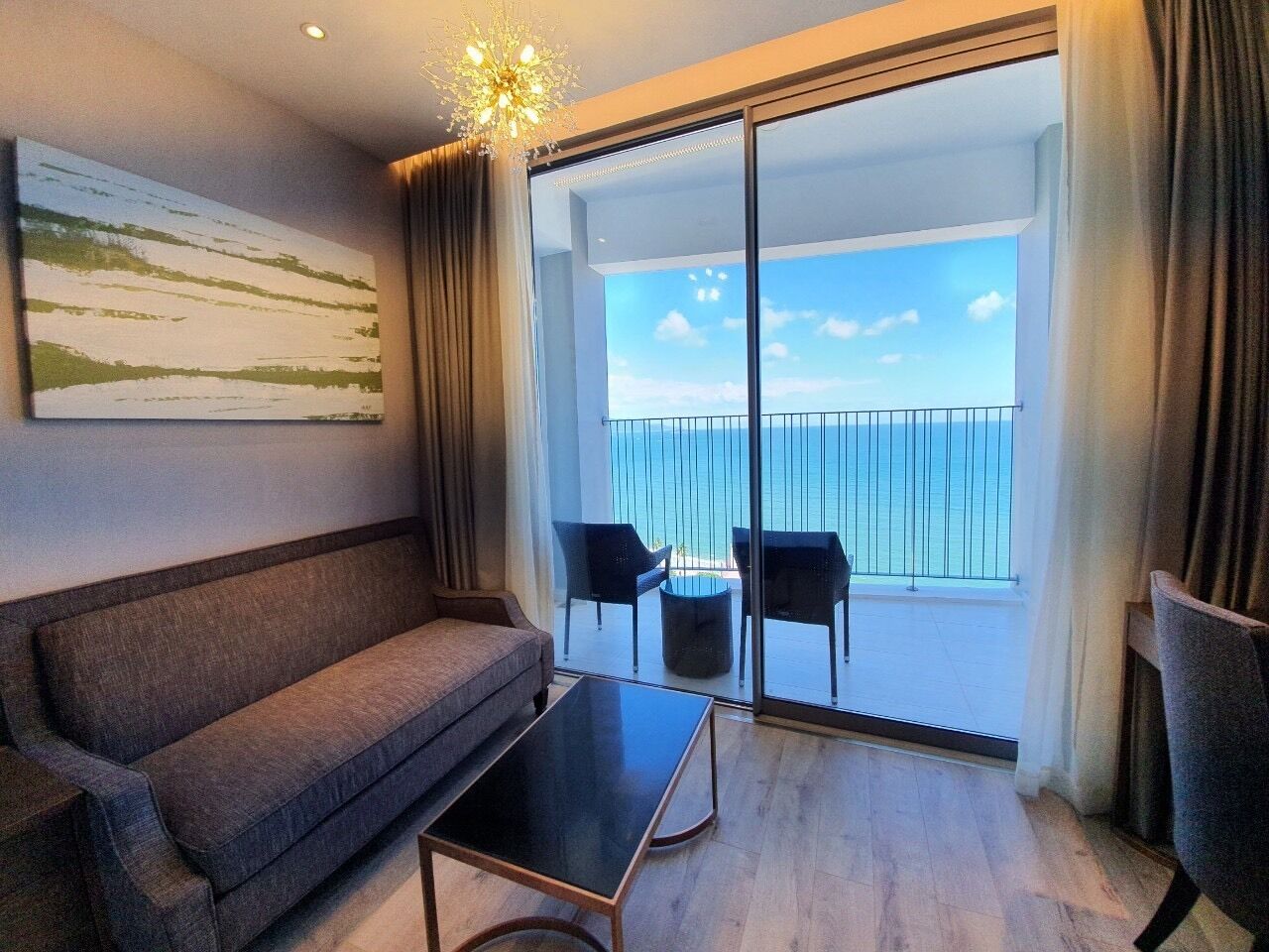 Une pièce comprenant un canapé, une petite table et deux chaises. Une grande fenêtre offre une vue sur la mer.