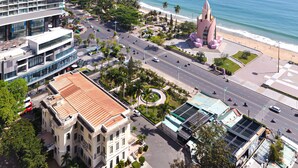 A coastal cityscape with a modern hotel, a beach, and a distinctive pink monument. - Holi Panorama Condotel (Nha Trang)