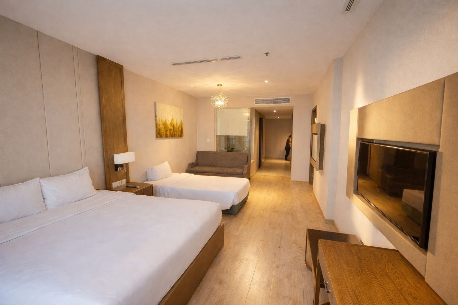 Habitación de hotel con dos camas, un sofá, un televisor y un pasillo que conduce a otra habitación.