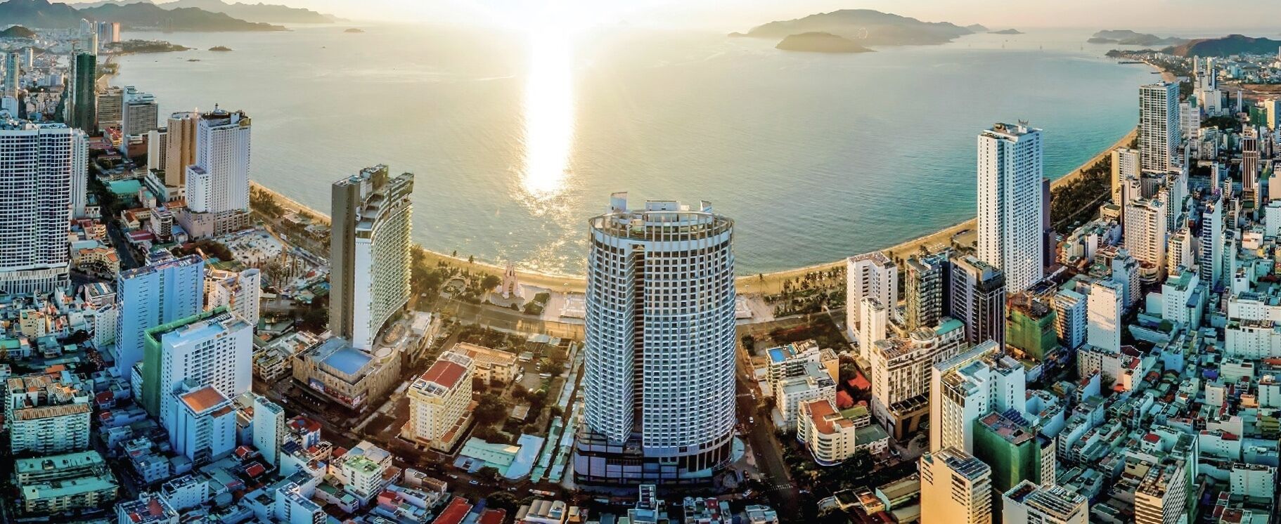 Un hotel moderno de altura con un patio central, rodeado de edificios urbanos y vistas al mar.