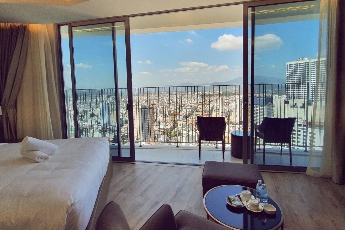 Een hotelkamer met een groot bed, een balkon met stoelen en uitzicht op de stad.