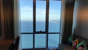 A hotel room with a large window offering a view of the sea and distant land. - Holi Panorama Condotel (Nha Trang)