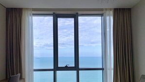 A room with a large window offering a view of the sea. There are two chairs and a small table with bottles. - Holi Panorama Condotel (Nha Trang)