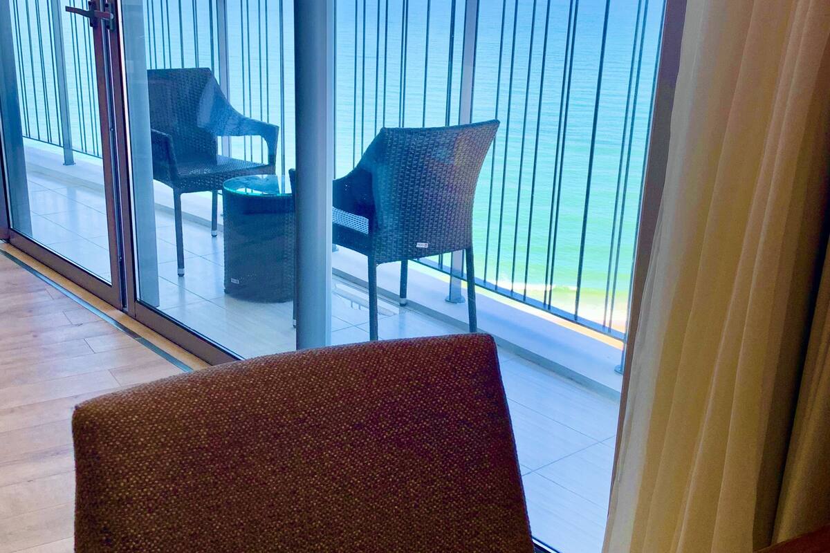 Een balkon met uitzicht op zee, met twee rieten stoelen en een kleine tafel.
