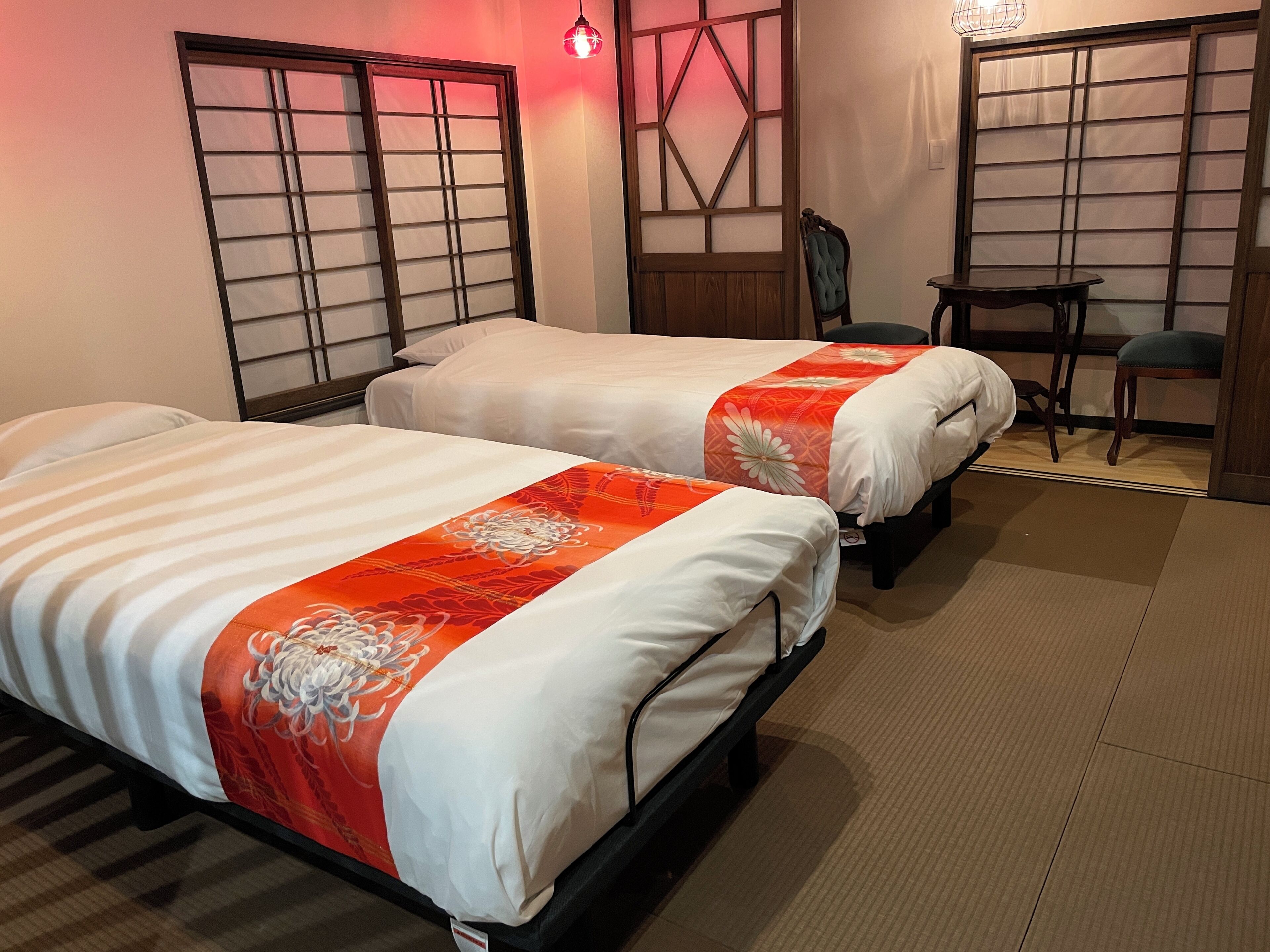 Two beds with white and orange bedding, a chair, and a small table in a room with traditional Japanese-style sliding doors and a wooden floor.
