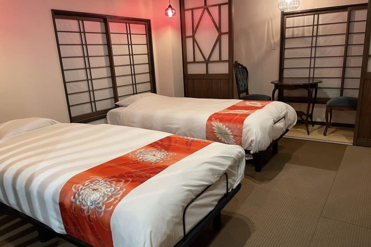 Une chambre d’hôtel avec deux lits, une chaise, une petite table et des portes coulissantes traditionnelles.