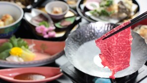 Une variété de plats sont disposés sur une table, dont une grande pièce de viande crue, présentée sur un plat et tenue à l’aide de baguettes.