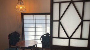 Une pièce de style japonais traditionnel, avec un sol recouvert de tatamis, un paravent en papier de riz (shoji), une table en bois et deux chaises.